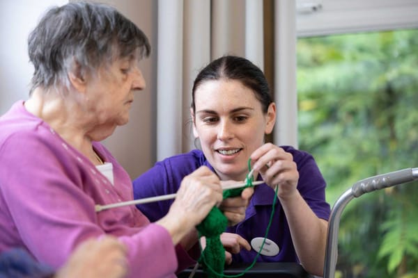 Staff member assisting a resident with knitting activity