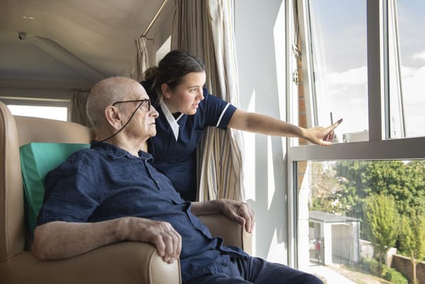 A caregiver assists an elderly resident by the window