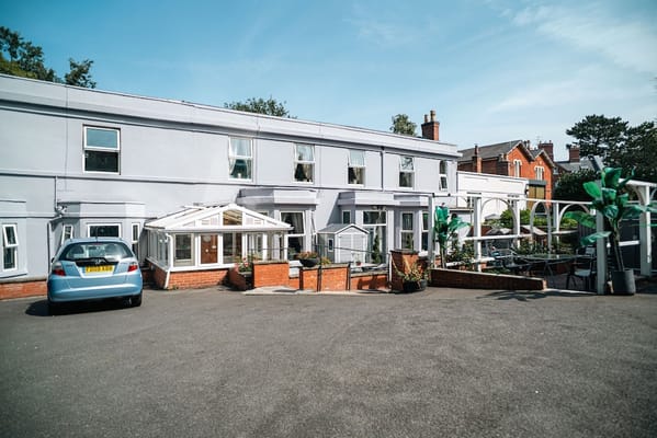 Exterior view of Forest Lodge Care Home with outdoor seating