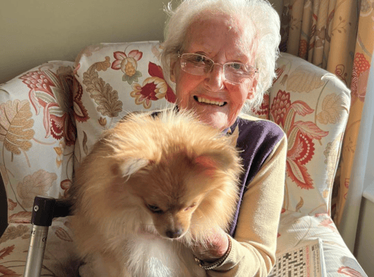 Senior resident smiling with a small dog in a cozy chair