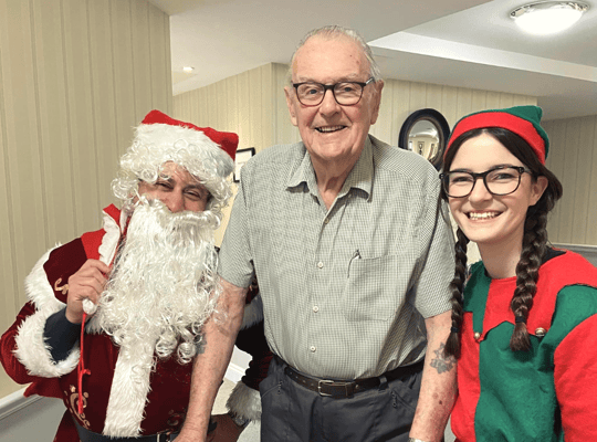 Resident posing with Santa and an elf during holiday celebrations