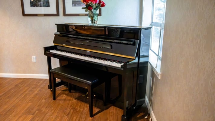 A piano in a cozy interior space with a vase of flowers