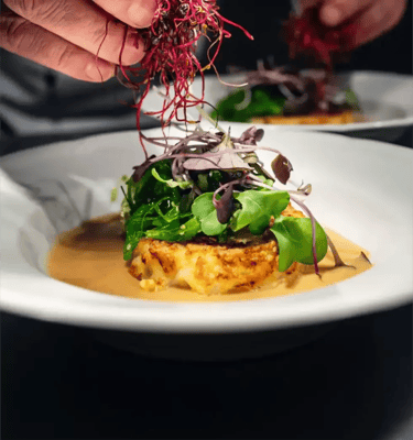 A chef garnishing a gourmet dish on a white plate