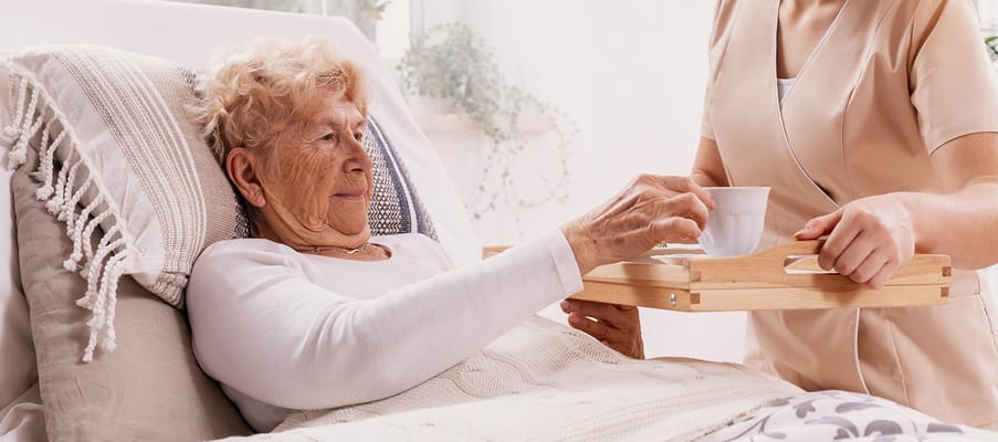 Caregiver serving tea to a senior resident in bed