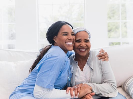 A caregiver and a senior resident smiling together on a couch