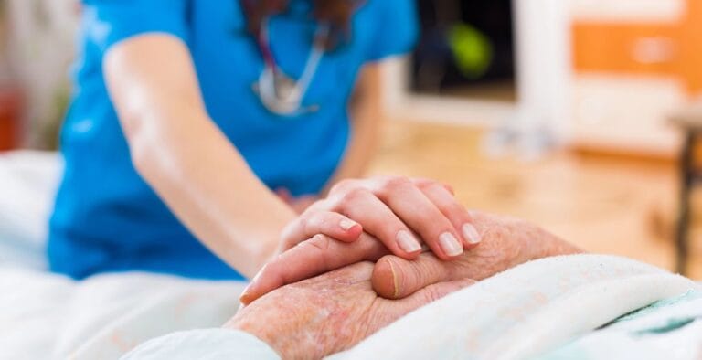 Healthcare worker gently holding an elderly patient's hand