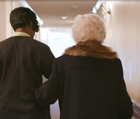 A caregiver assisting an elderly resident in a hallway