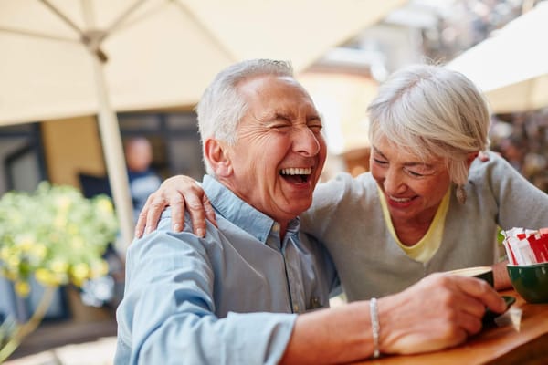 Two seniors enjoying a laugh outdoors at a table