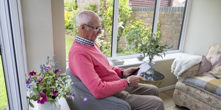 An elderly man reading in a sunlit common area