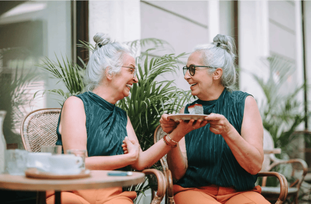 Two elderly women laughing and sharing food on a patio