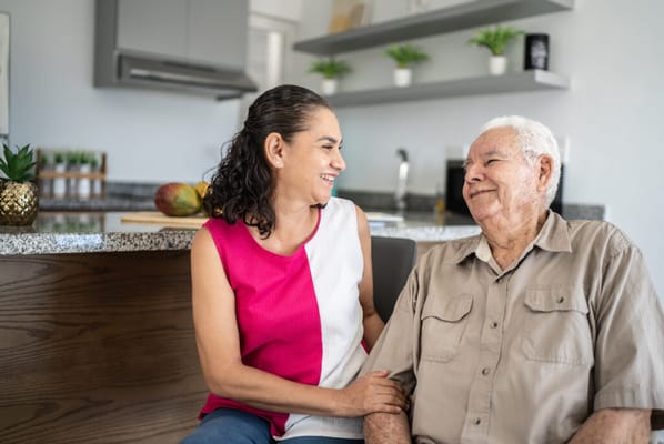 A caregiver smiling at an elderly man in a bright kitchen