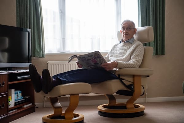 An elderly man reading a newspaper in a comfortable chair