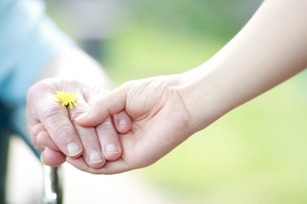 Hands of a resident and caregiver holding a flower