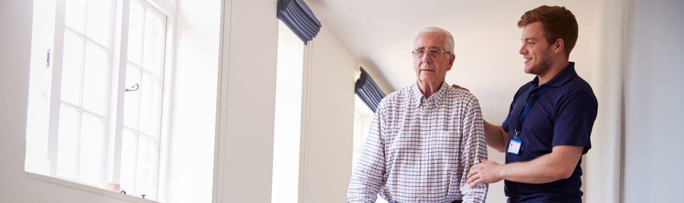 A staff member assisting an elderly resident in a facility hallway