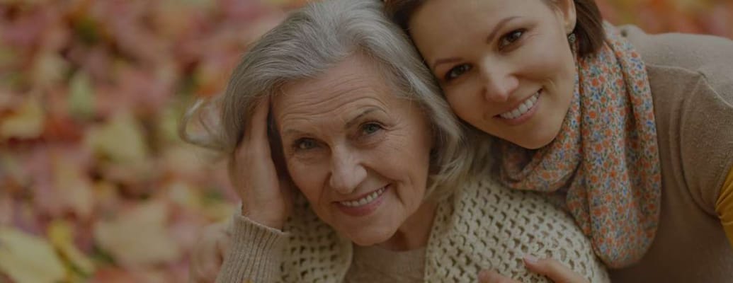 A senior woman and a caregiver smiling in autumn leaves