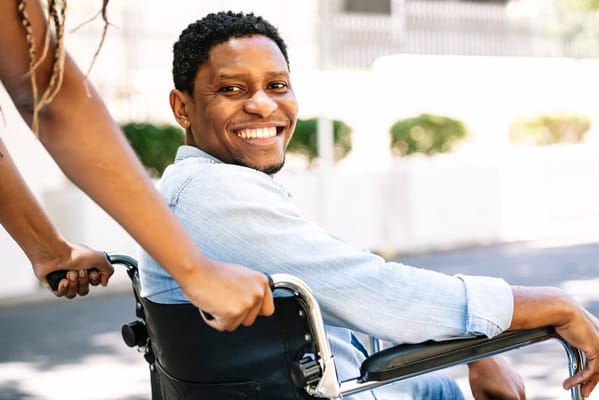 A smiling resident in a wheelchair being assisted outdoors