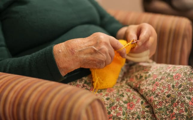 Close-up of elderly hands knitting a yellow piece
