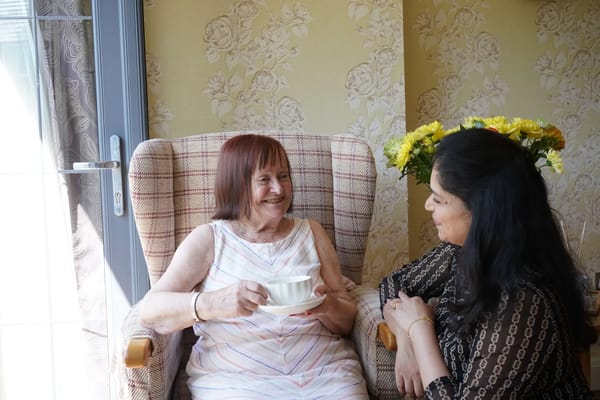 Resident enjoying tea with a staff member in a cozy setting