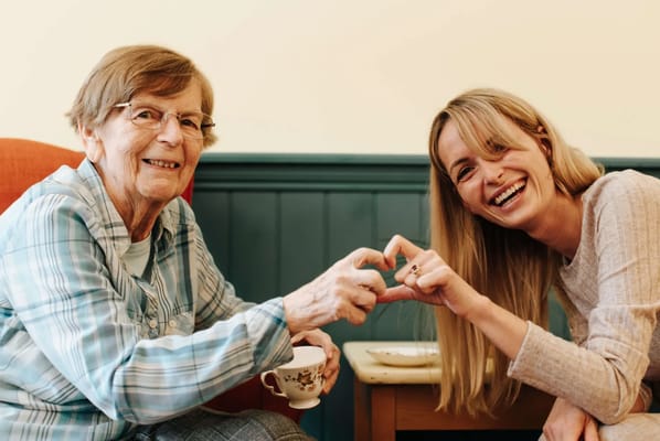 Elderly resident and staff member making a heart with their hands