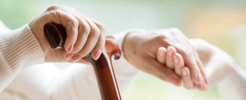 Hands of a resident resting on a cane and another hand