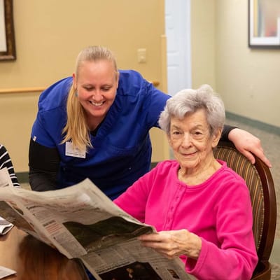 A staff member assisting a resident with a newspaper