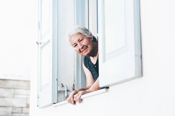 Senior woman smiling at a window, representing community life