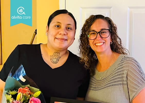 Two staff members celebrating with flowers and a framed certificate