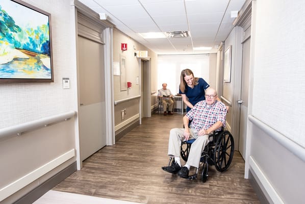 A caregiver assisting a resident in a wheelchair in a hallway