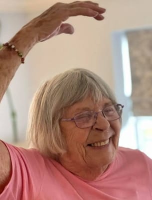 An elderly woman smiling with her hand raised