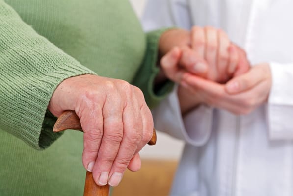 Close-up of an elderly person holding a cane and caregiver's hand