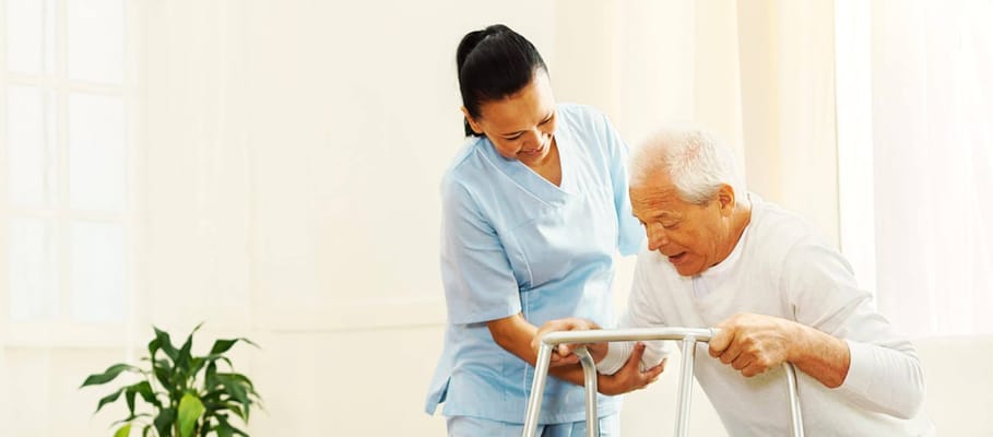Caregiver assisting an elderly man with a walker in a bright room