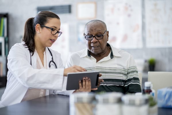 A healthcare worker assisting an elderly man with a tablet.