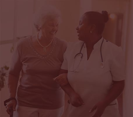 Senior resident walking with a caregiver in a hallway