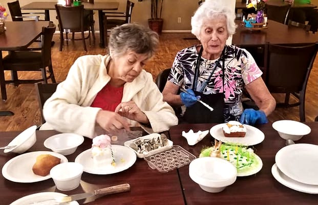 Two residents decorating desserts at a dining table