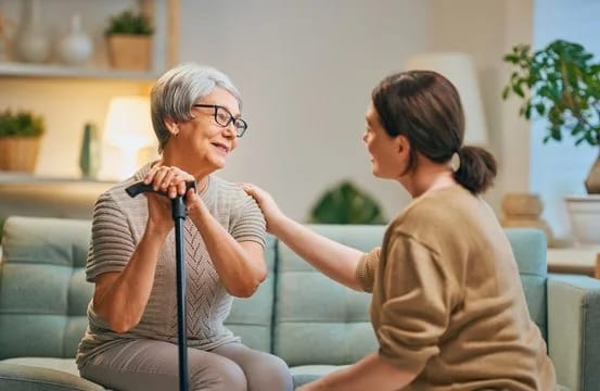An elder woman conversing with a caregiver in a cozy lounge.