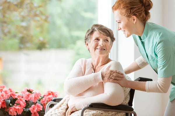 Staff member assisting a smiling resident in a bright room
