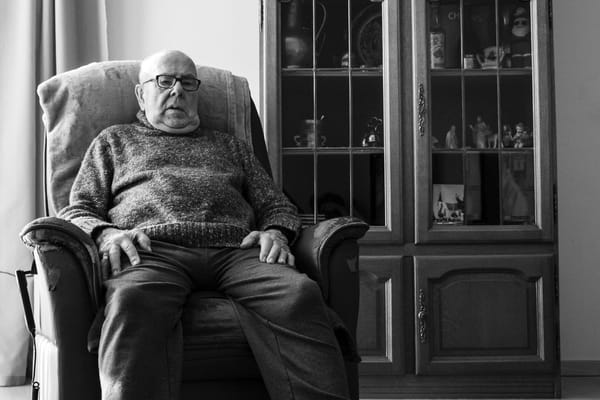 An elderly man seated in a cozy chair inside a common area