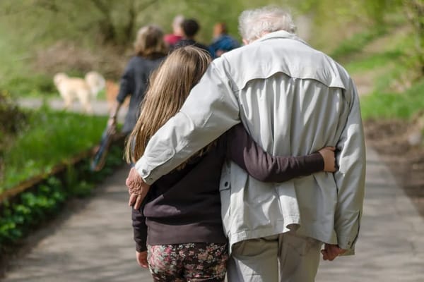 An elderly man walking with a young girl on a path