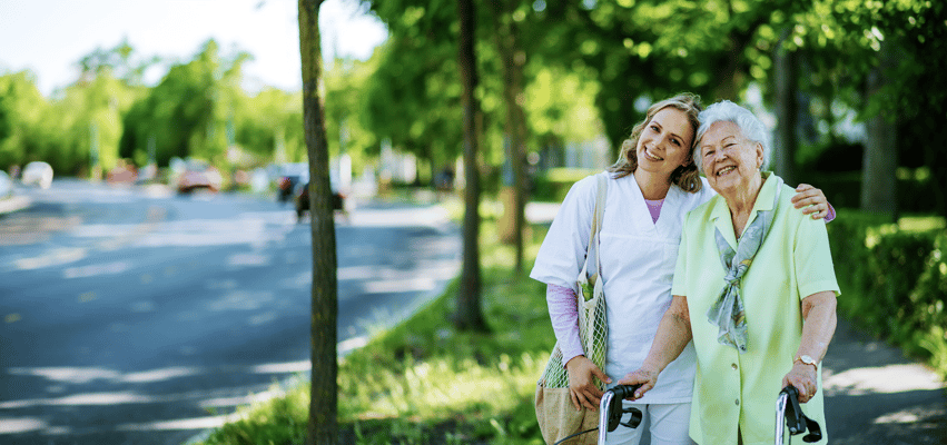 Caregiver assisting a smiling senior woman outdoors