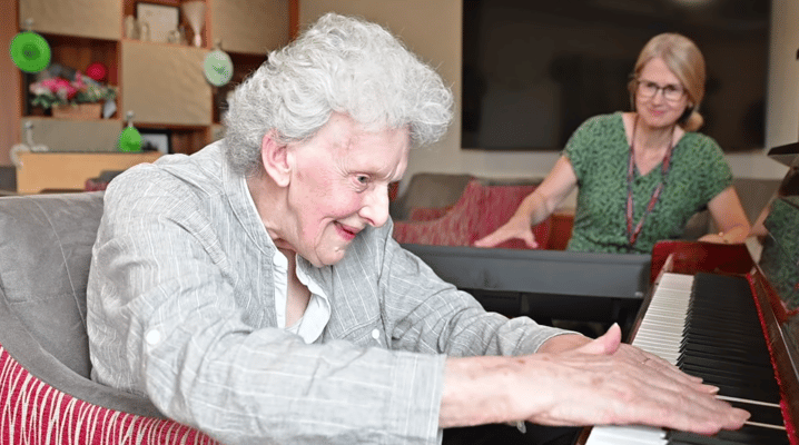 Resident enjoying music on a piano with staff support