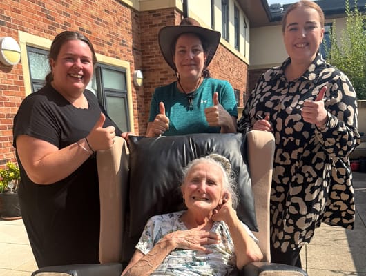 Residents and staff smiling and giving thumbs up in outdoor space