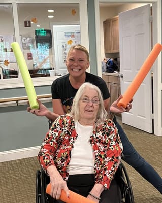 Resident and staff smiling with foam pool noodles