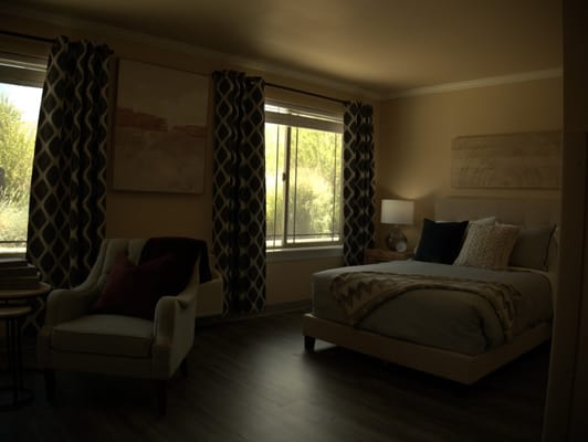 Well-furnished bedroom with a bed, chair, and large windows.