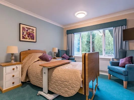 A well-furnished bedroom with a bed, armchairs, and natural light.