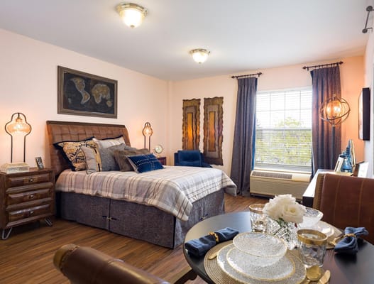 Stylish bedroom with a bed, nightstand, and dining table at Belmont Village Senior Living