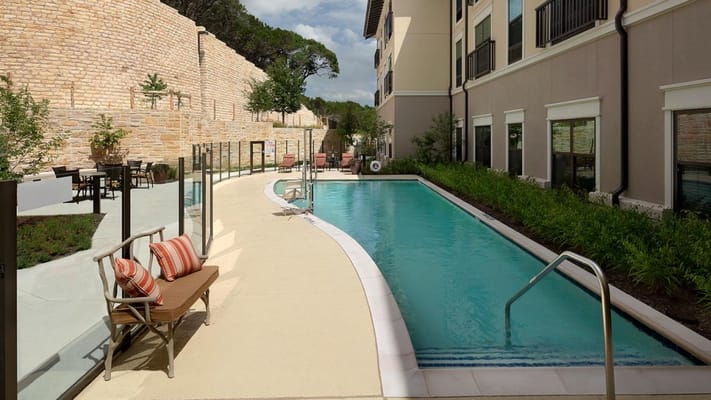 Outdoor swimming pool with lounge chairs and a landscaped area in a senior living facility