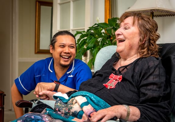 Resident and staff member sharing a laugh in a cozy setting.
