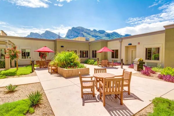 Sunny courtyard with seating and red umbrellas at Catalina Springs Memory Care