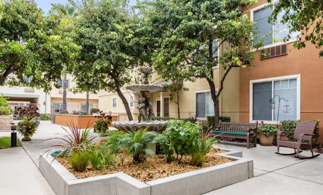 A courtyard with a fountain surrounded by greenery and benches.