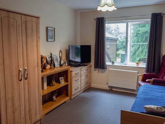 A cozy bedroom with a tv, dresser, and large window